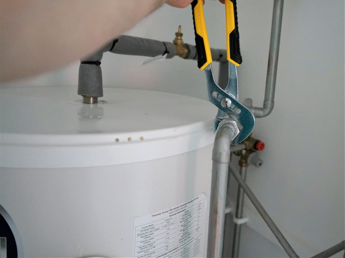 Intervention sur un chauffe-eau, pince multiprise en main.